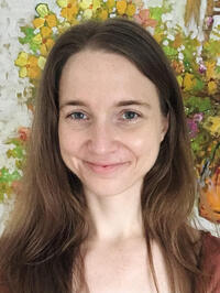 White female with long reddish-brown hair and gray eyes smiling in front of a floral background.