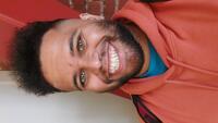 Young man with hazel eyes and big smile wearing an orange hoodie. 